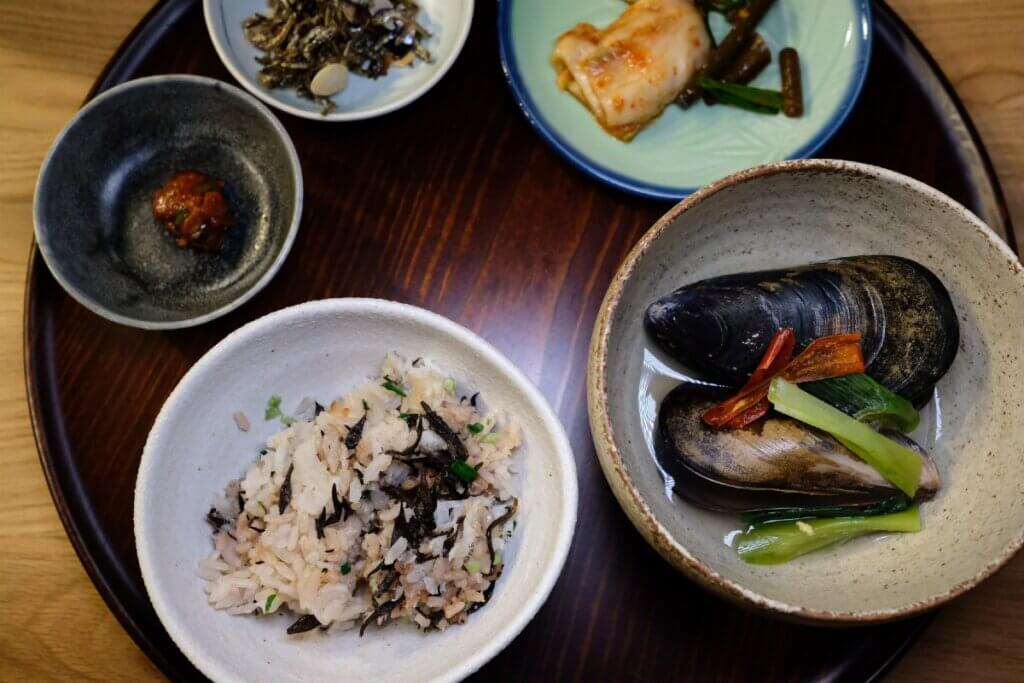 5 bowls of home-cooked Korean cuisine, including a rice dish, kimchi and mussles.