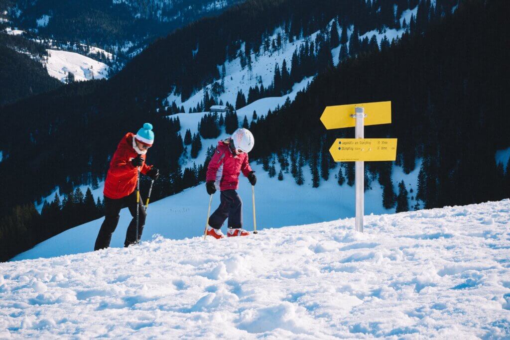 A parent and child in ski gear walking up a slope while on a ski holiday