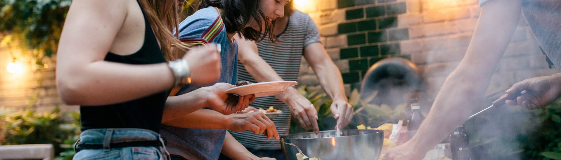 A young group of friends are helping themselves to freshly prepared food at a summer evening Barbecue.